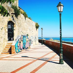 Street light on footpath by sea against clear sky