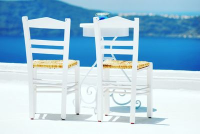 Close-up of white empty chairs on terrace at santorini
