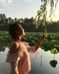 Side view of woman standing by lake against sky