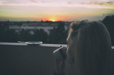 Teenage girl drinking coffee sitting at terrace during sunset