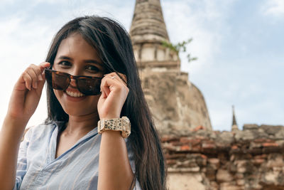 Portrait of beautiful young woman holding umbrella against sky