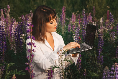 Young woman using phone while standing by purple flowers