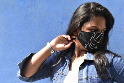 Portrait of young woman standing against blue wall