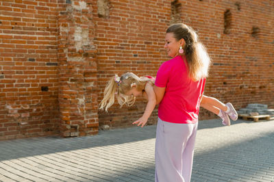 Portrait of young woman standing against brick wall