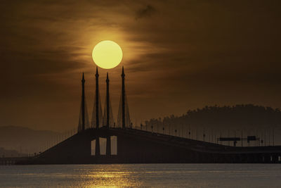 Silhouette penang bridge over sea against sky during sunset
