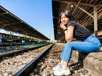 Full length portrait of girl sitting by railroad tracks