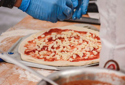 Hands with plastic gloves adding fresh mozzarella on a pizza with tomato sauce on a wooden board