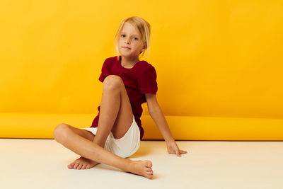 Girl sitting on floor against yellow backdrop