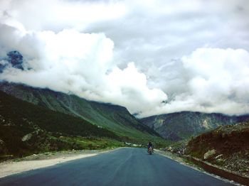 Man riding motorcycle on road amidst mountains against sky