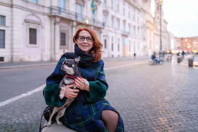 Woman sitting on the bench she happily hugs her chihuahua dog. in the city of rome, italy.