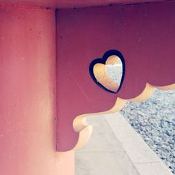 Close-up of hand holding heart shape on pink wall