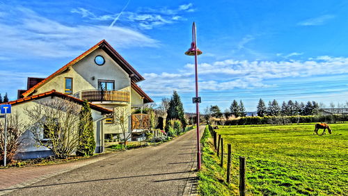 Footpath amidst houses on field against sky