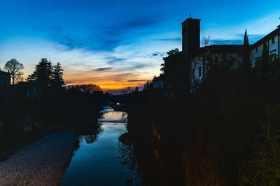 Silhouette trees by river against sky during sunset