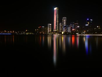 Illuminated buildings by river against sky at night