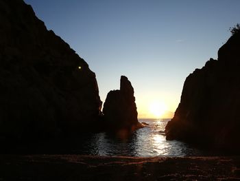 Silhouette rocks by sea against clear sky during sunset