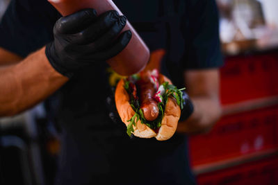 Midsection of man pouring sauce on hot dog at street