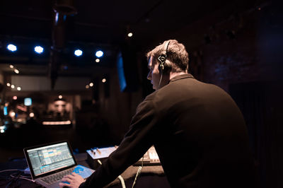 Rear view of man using laptop while standing in nightclub