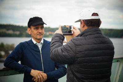 Rear view of man photographing friend with smart phone