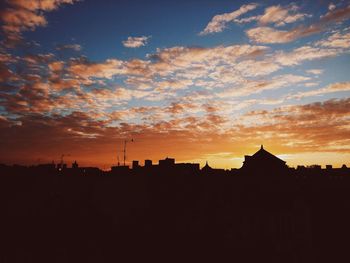 Silhouette buildings against cloudy sky during sunset in city