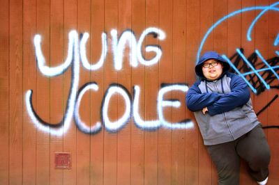 Overweight teenage boy standing against graffiti wall