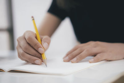 Midsection of student writing on book at table in classroom