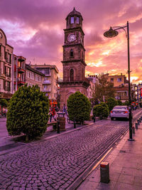 Street amidst buildings against sky at sunset