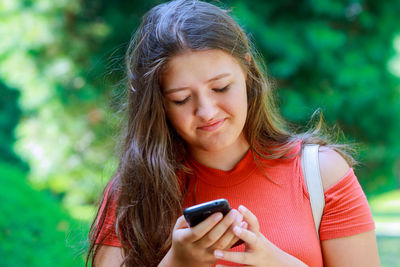 Young woman using mobile phone while standing against trees at park