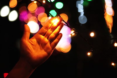 Cropped hand of person touching illuminated string light at night