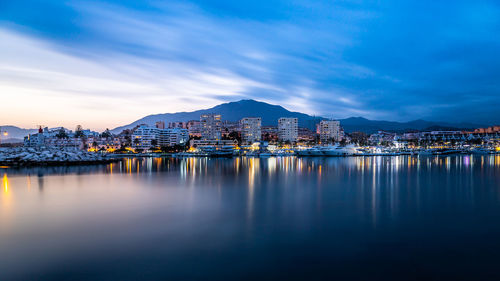 Illuminated buildings by lake against sky in city