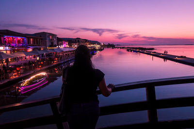 Rear view of woman standing by railing against sky during sunset