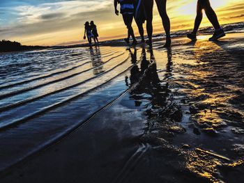 People walking on shore at beach during sunset