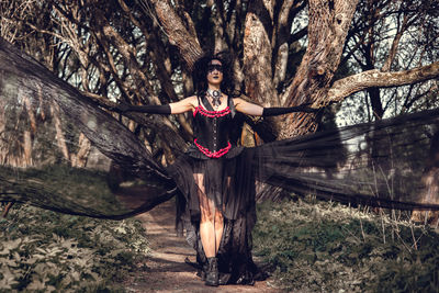 Full length of woman standing by tree trunk