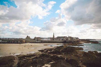 Scenic view of beach by buildings against cloudy sky