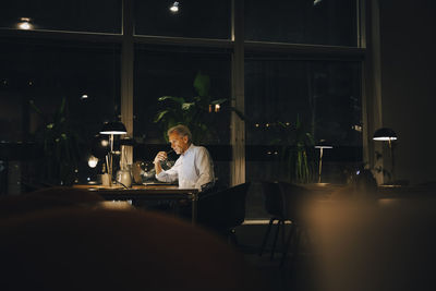 Thoughtful businessman working late while sitting with laptop in dark workplace