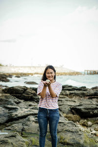 Smiling young woman holding stone while standing on rock at beach