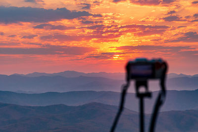 Shadow of camera on mountain against sky during sunset