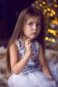 Baby girl sitting in studio in dress with christmas tree in christmas with long hair