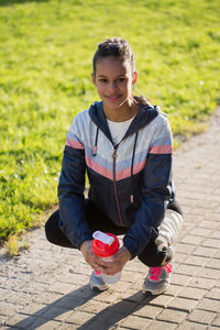 Full length portrait of young woman crouching on footpath