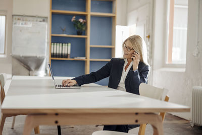 Businesswoman using laptop and cell phone in office
