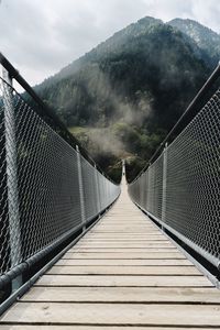 Footbridge against mountain and sky during foggy weather