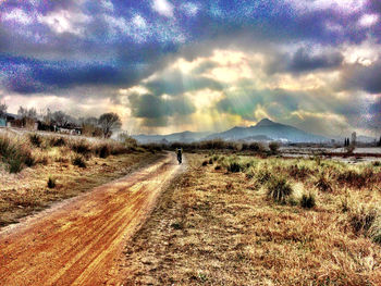 Road passing through field against cloudy sky