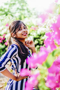 Portrait of beautiful young woman standing against pink flowering plants