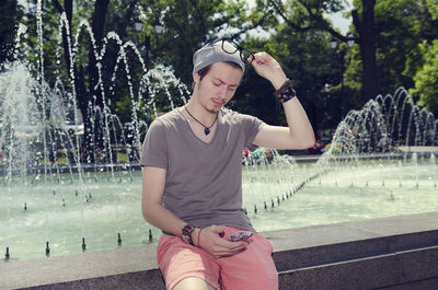 Young man using mobile phone against fountain at park