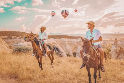 Couple sitting on horses against hot air balloons flying in mid-air