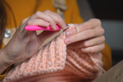 A young caucasian woman in casual home clothes knits a pink wool hat or scarf. a useful hobby is