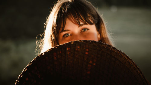 Close-up portrait of a beautiful young woman holding a straw hat at sunset