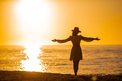 Silhouette woman standing at beach during sunset