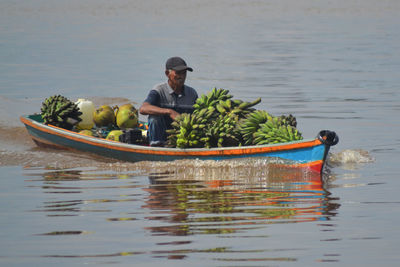 Man with fruits sitting on boat in lake