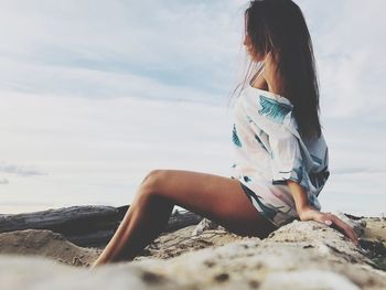 Side view of woman wearing swimwear while sitting at beach against sky