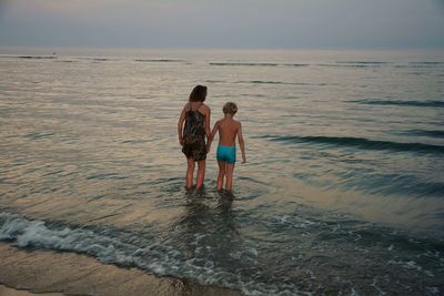 Mother and son wading in sea during sunset